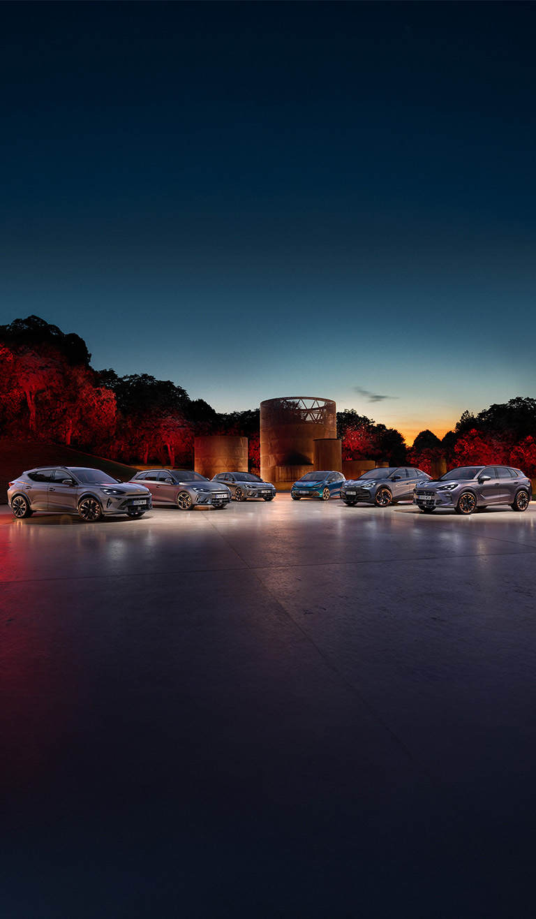 A person intently looking at their smartphone, standing outdoors with blurred modern city buildings and a bright sunset sky in the background.