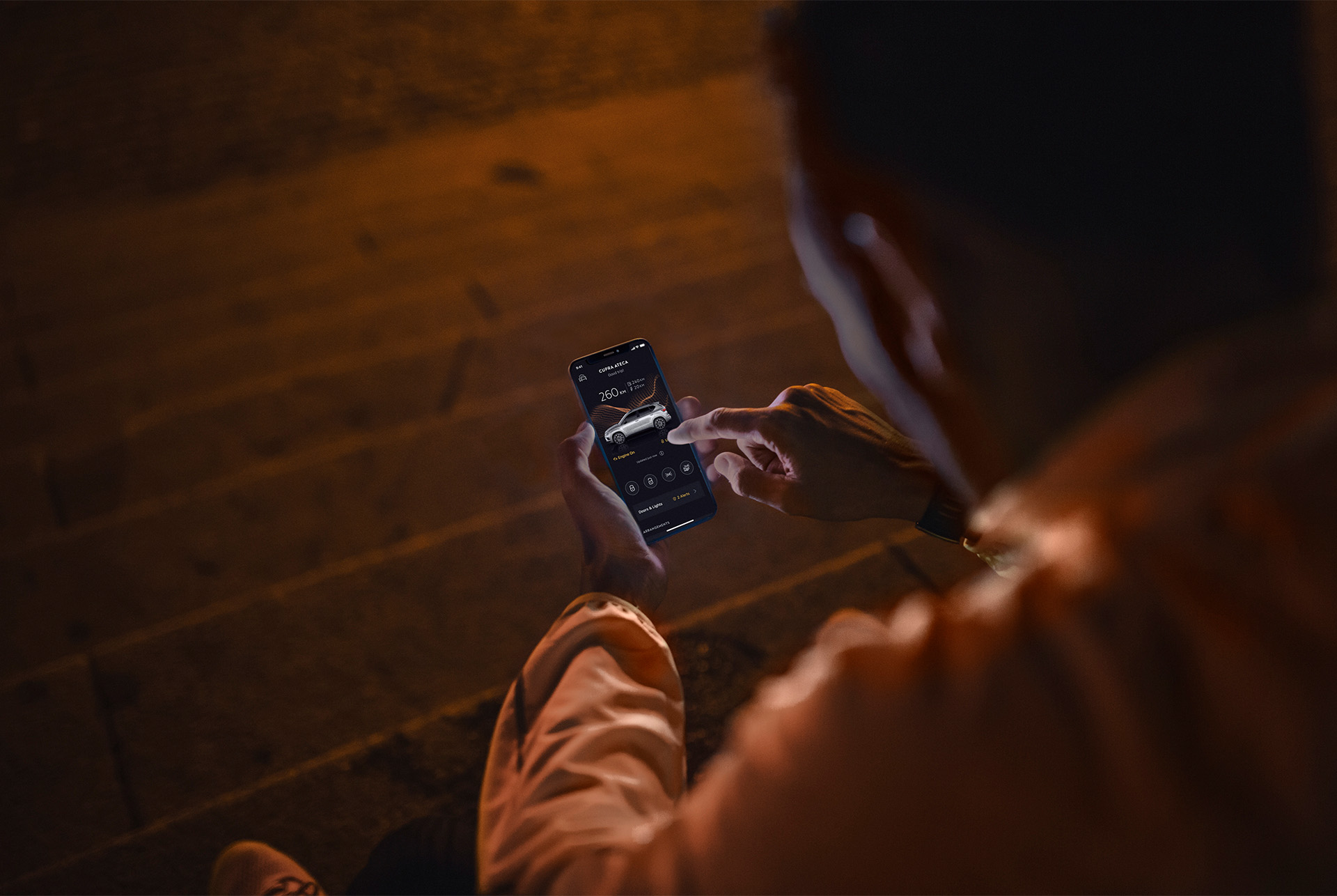 CUPRA CONNECT online services incorporates a range of solutions to answer to the challenges of modern life. A person sitting on stairs at night, using a smartphone illuminated by the screen.