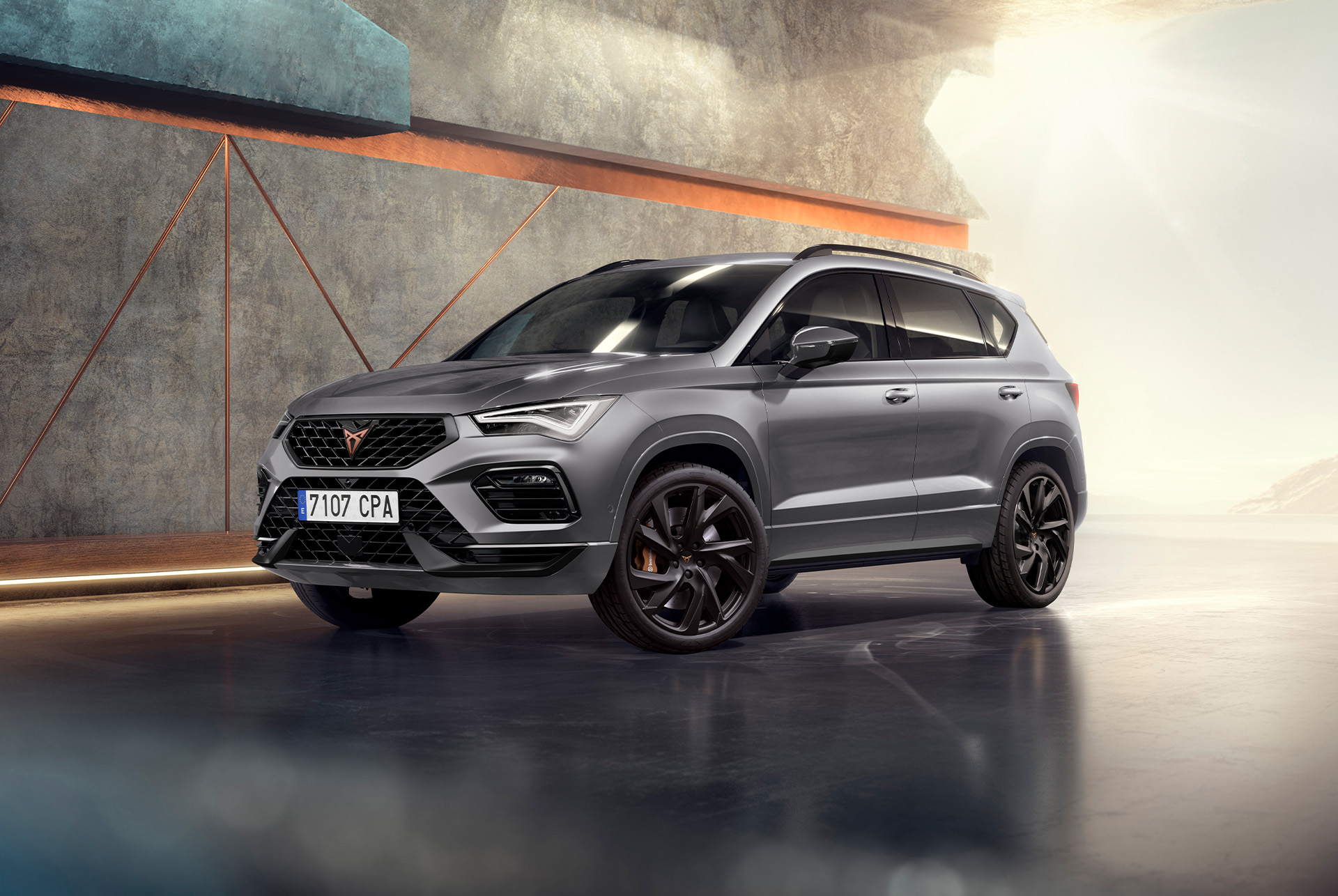 A 2025 cupra ateca in graphite grey, a sporty and compact suv parked in a modern, industrial setting. The car design features aerodynamic lines, led headlights and distinctive alloy wheels with copper accents. The background includes a geometric wall design, contrasting with the sleek vehicle design.