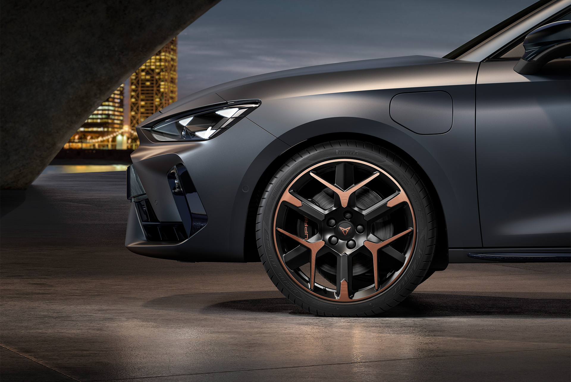 front side view of left forged alloy wheel in copper and black for the Cupra Leon, tyres, signature headlights and matt grey body.