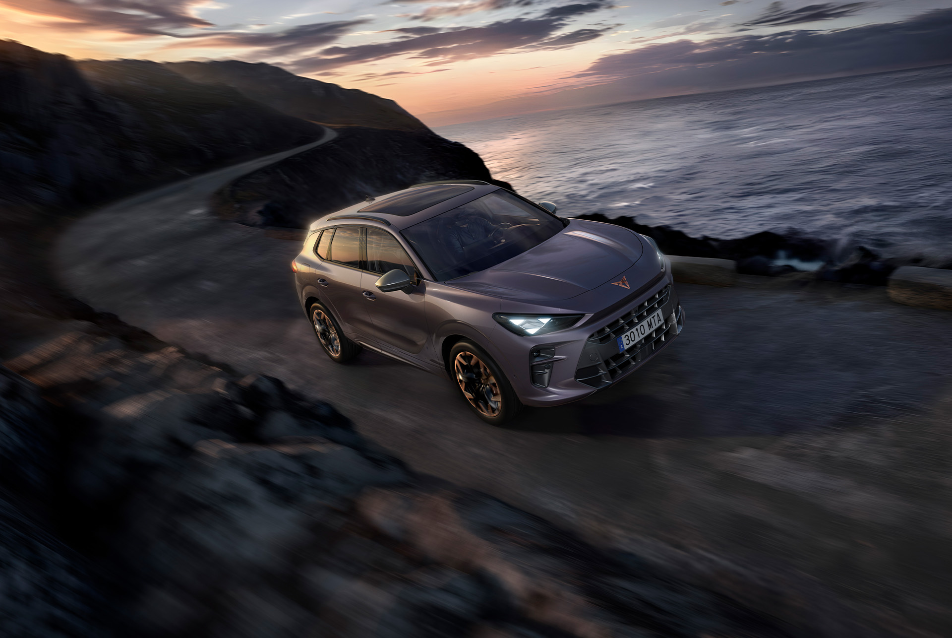 CUPRA Terramar 2025, with dynamic chassis control (DCC), driving along a coastal road featuring dark void paint, and 20” hadron copper alloys.