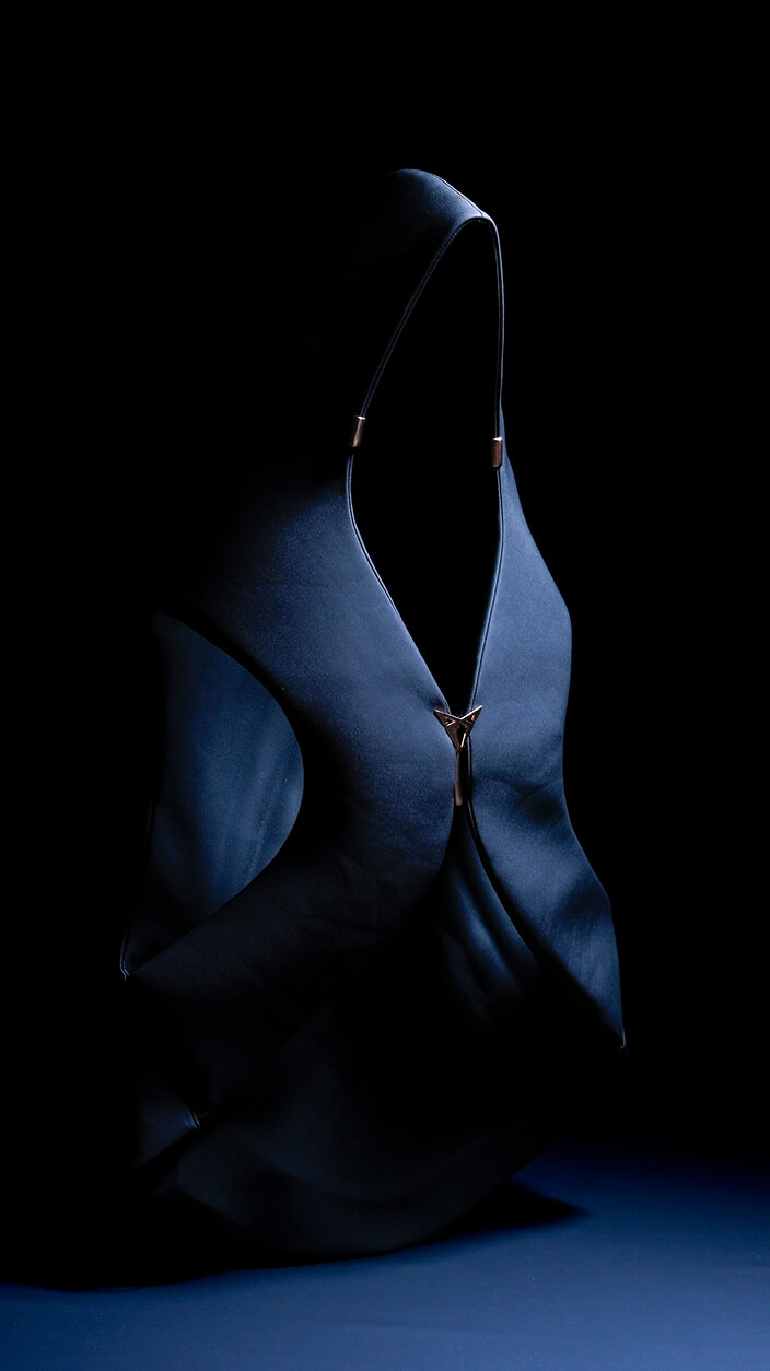 A minimalist image featuring a person wearing a dark hooded garment with subtle metallic details, against a black background.