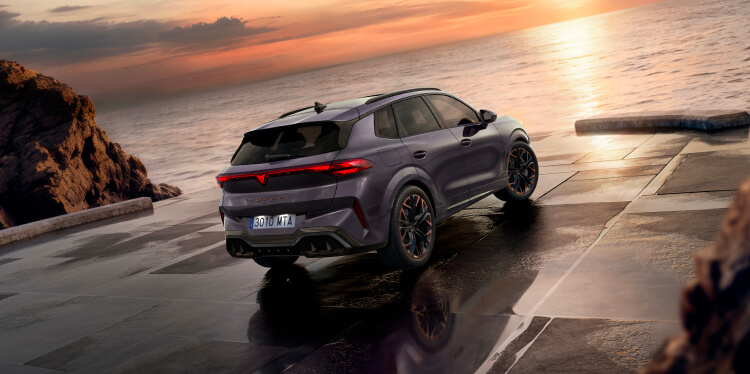 Rear view of a new cupra terramar parked in front of the sea, looking at the sunset.