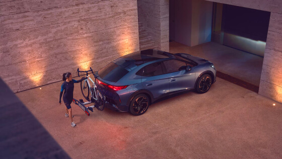 A person loading a bike onto a cupra tavascan parked in a modern driveway, showing the EV’s versatility for active lifestyles.