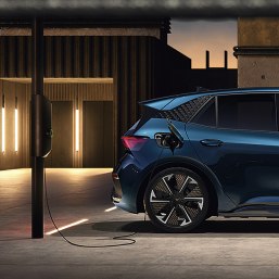 electric car cupra leon charging in car park with wall charger, ambient lighting, concrete and sky