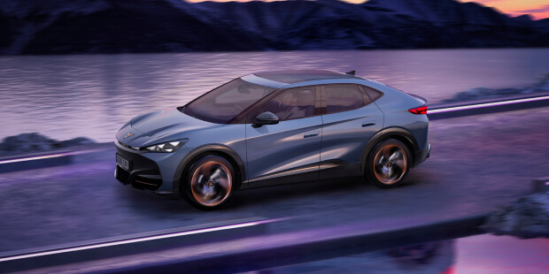 A cupra tavascan electric car driving along a futuristic coastal road at dusk, with calm waters and silhouetted mountains in the background.
