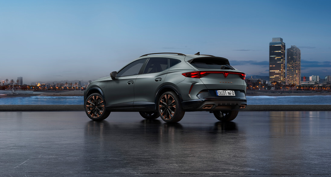 A cupra formentor parked in an outside parking, in the dark with a view of the city in the back.