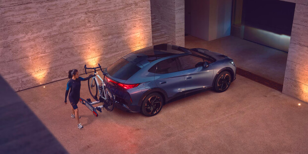 A person loading a bike onto a cupra tavascan parked in a modern driveway, showing the EV’s versatility for active lifestyles.