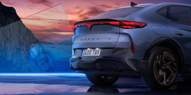 Rear view of a cupra tavascan electric SUV parked on a reflective surface with mountains and a colourful sunset sky in the background.